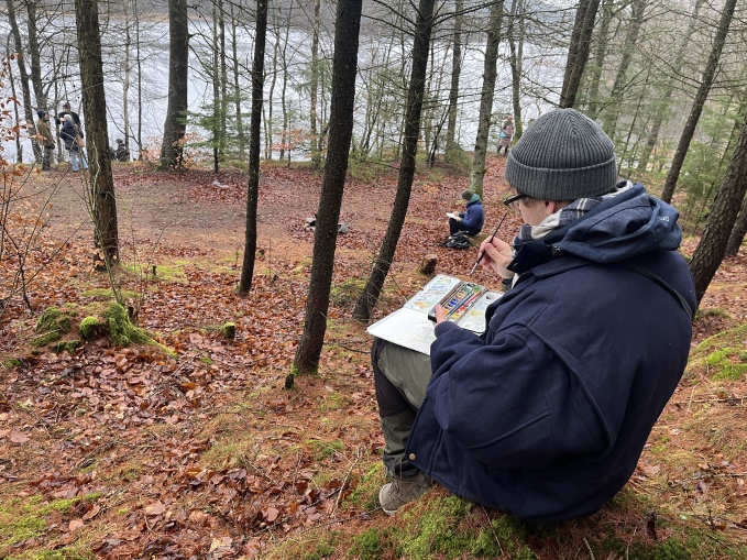 Person sitter i naturen och målar av området med akvarell