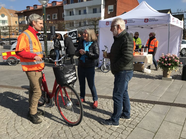 Tre personer står och pratar vid en elcykel