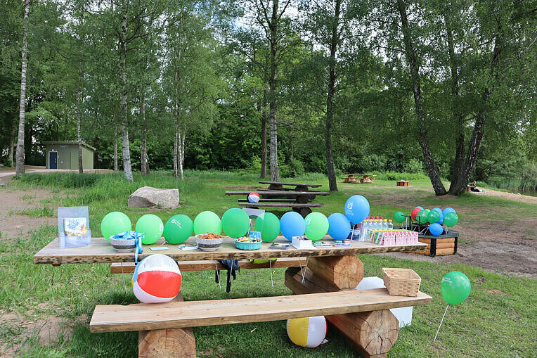 Bänk dekorerad med ballonger i kommunens färger. På bordet finns bubbelvatten, festis och godis. 